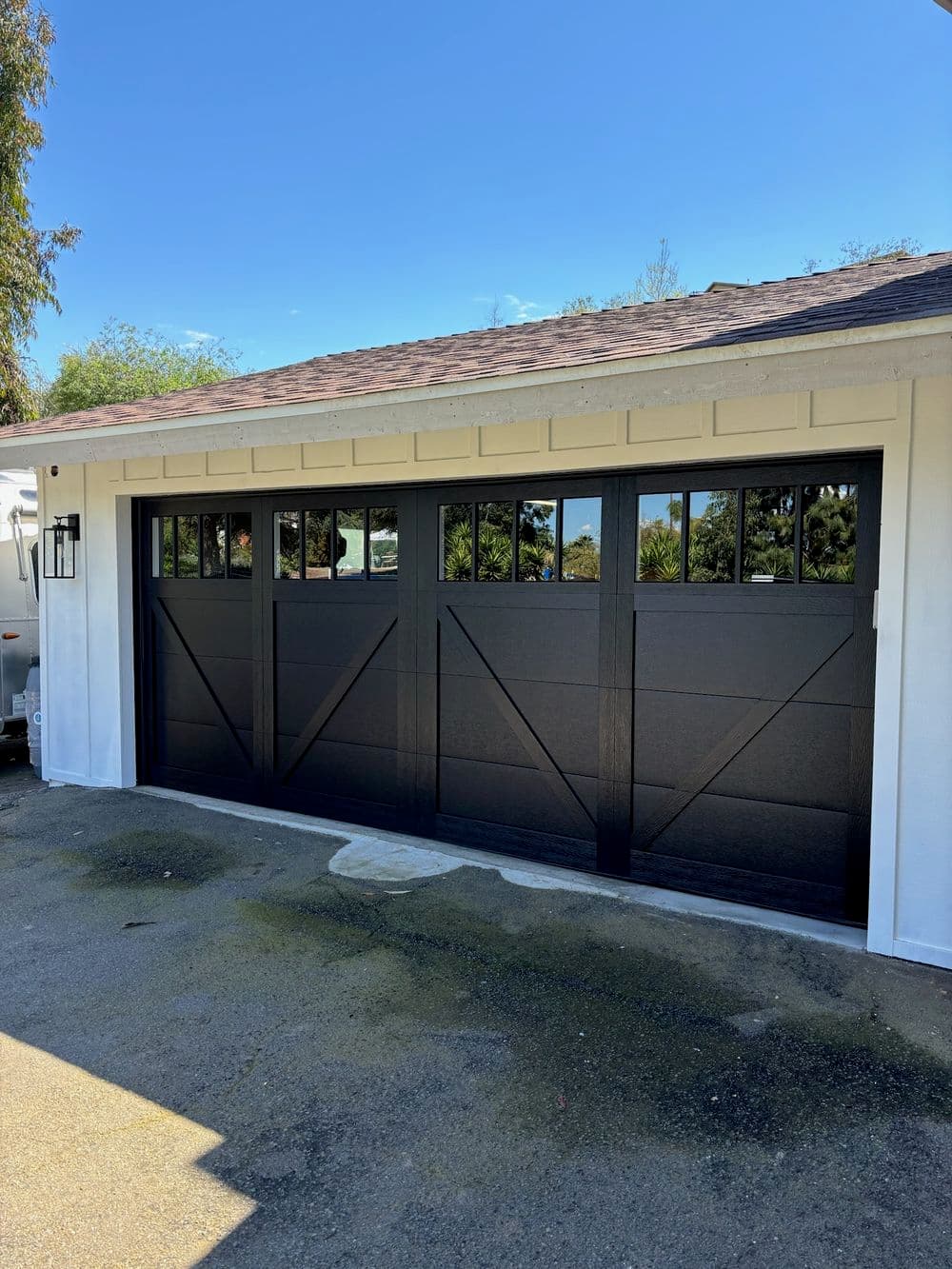 Modern black garage door with decorative windows on a white house exterior.