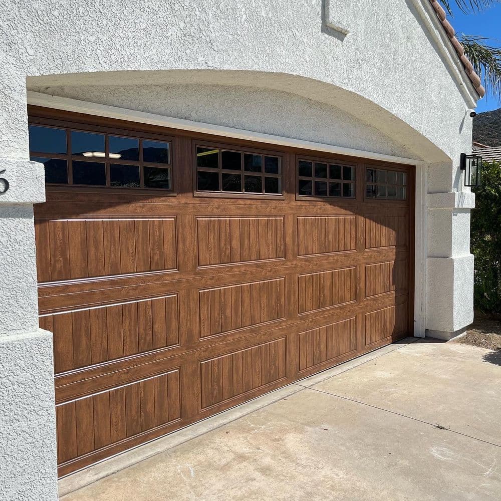 Wooden garage door with decorative windows on a white stucco house exterior.