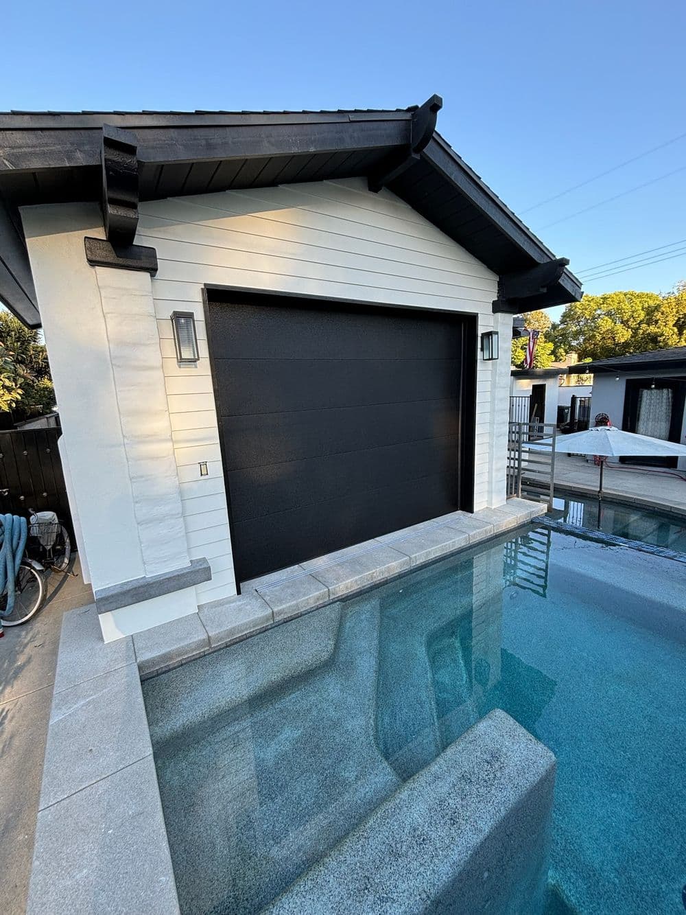 Modern garage door beside a swimming pool, featuring a sleek design and stylish lighting.