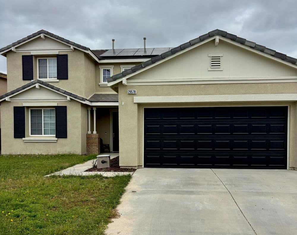 Modern two-story home with solar panels, black shutters, and a large garage door.